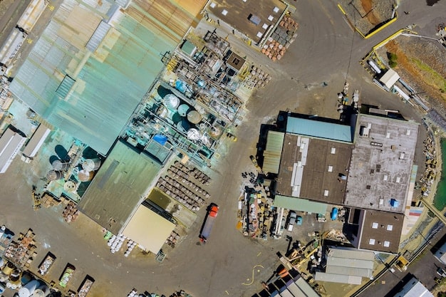 An aerial view of a large battery manufacturing plant in the United States. The image shows the scale of the facility, with hundreds of shipping containers and trucks moving materials in and out.