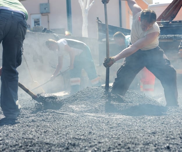 A construction site using recycled aggregate concrete, showing workers pouring and leveling the material.