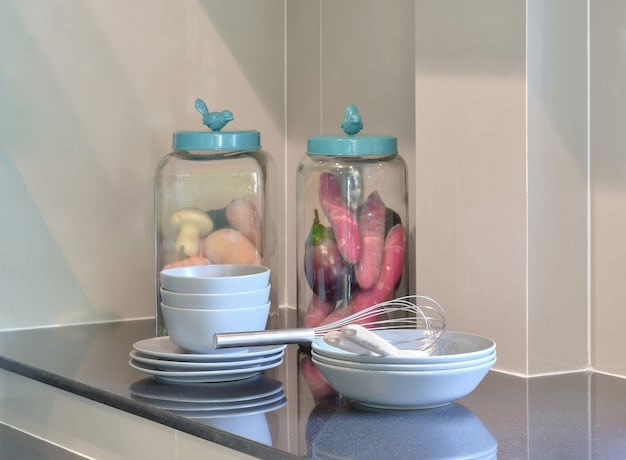 A brightly lit kitchen counter featuring a variety of reusable food storage options, including glass containers, beeswax wraps, and silicone bags. Fresh fruits and vegetables are visible inside some containers, showcasing their practicality.
