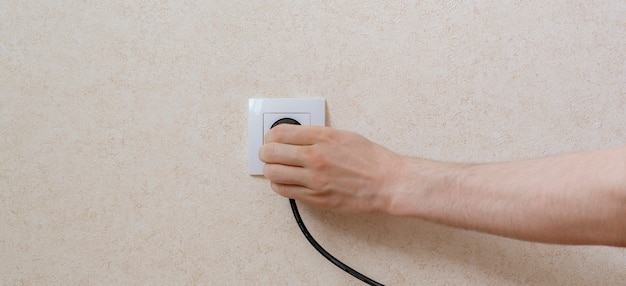 A close-up of a hand unplugging a device from a power outlet, with a focus on the energy-saving aspect of reducing phantom load.