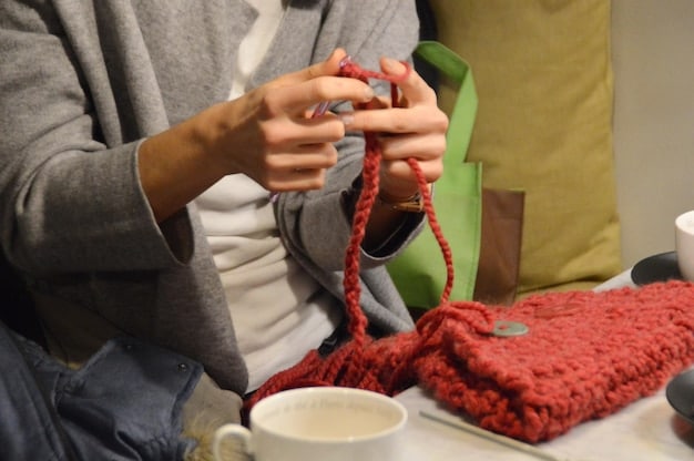 A person crafting a DIY gift, such as knitting a scarf with organic yarn, assembling a terrarium in a recycled glass jar, or creating a beeswax wrap for food storage. The scene focuses on the hands and the crafting process, emphasizing the personal touch and creativity involved in DIY gift-giving.