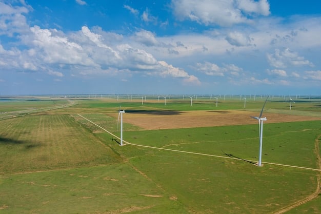 A detailed view of a modern wind turbine farm in a rural area of the US, with clear blue skies and green fields. Several turbines are actively spinning, generating electricity.