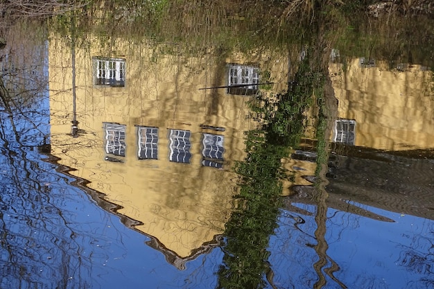 A flooded residential street with houses submerged up to their windows. Cars are partially underwater, and residents are wading through floodwaters. The sky is overcast, indicating ongoing rainfall.